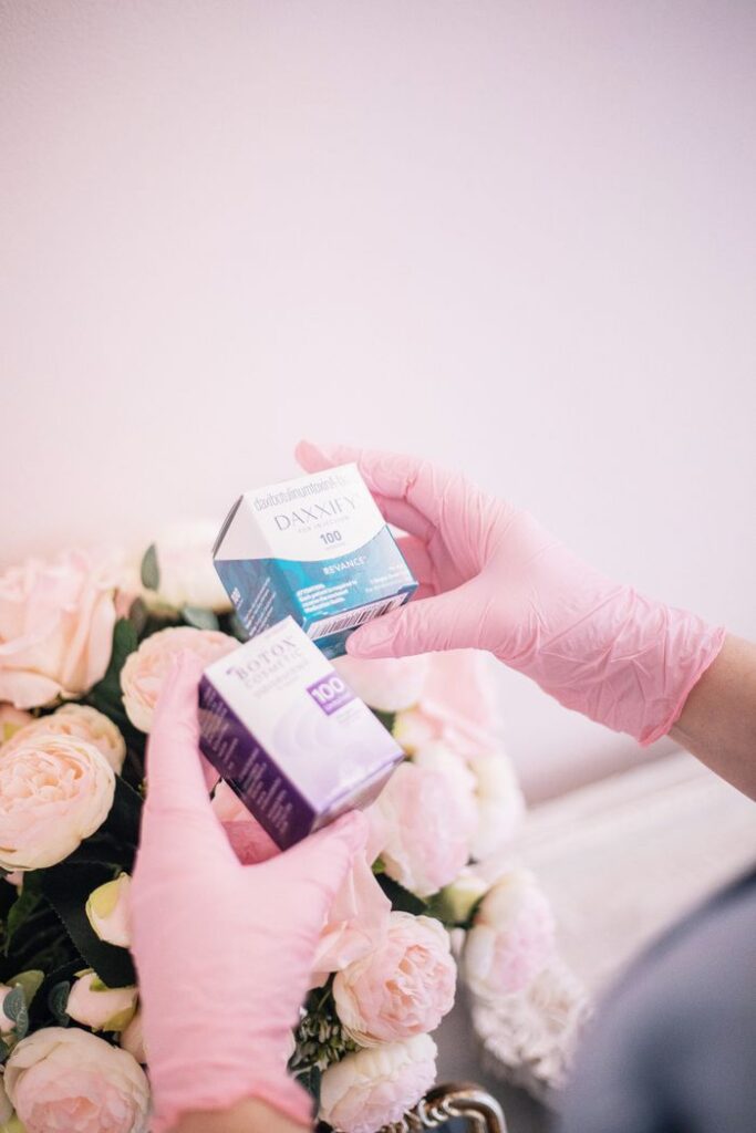 About Pink gloved hands holding beauty products with roses in a spa setting.